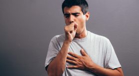 man coughing into fist and holding chest