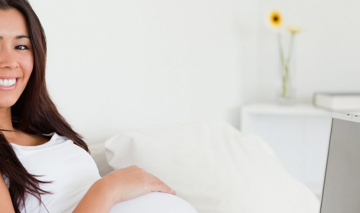 pregnant woman lying on bed with laptop