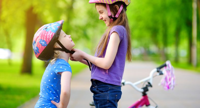 Girl helping younger sister with bike helmet strap