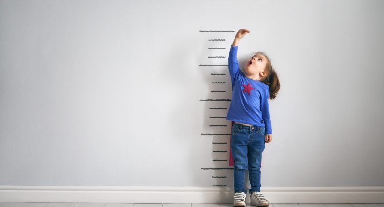 Little girl measuring herself against wall ruler