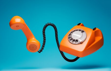 Orange rotary telephone with receiver off the hook floating in air