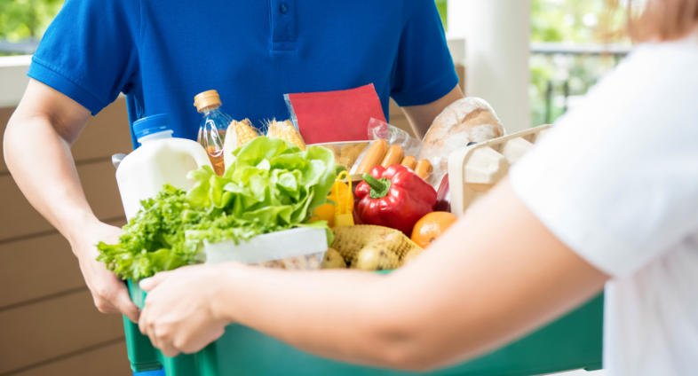 woman receiving box of fresh vegetables from delivery man